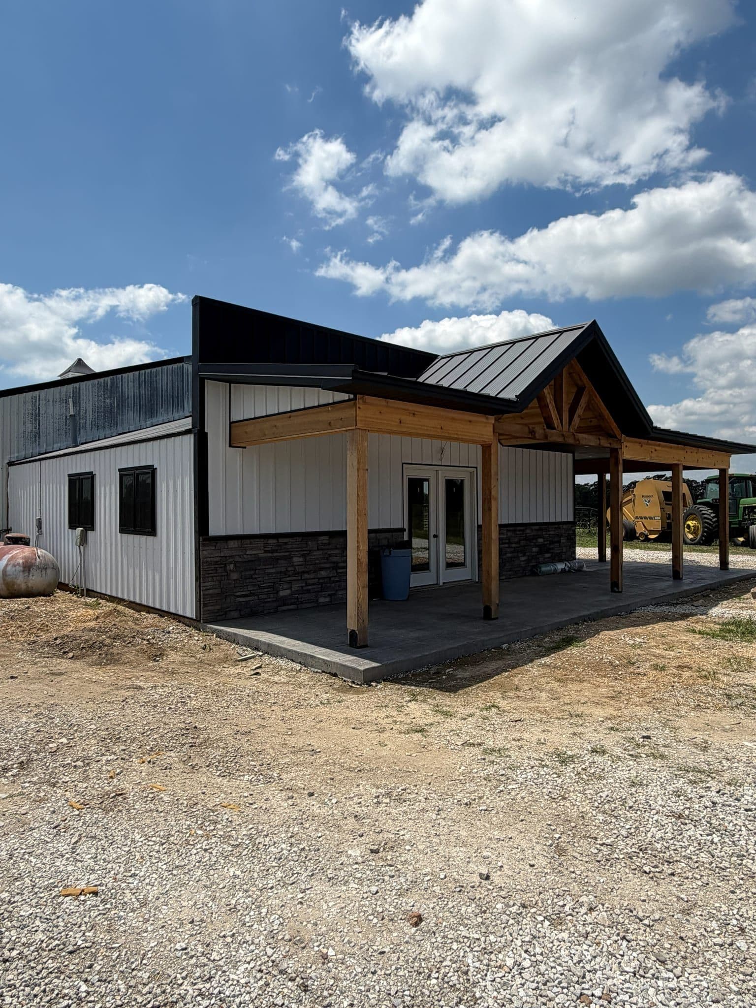 Corner of a post-frame building by Efficiency Construction — cedar timber-frame porch, stone wainscot, black standing-seam roof
