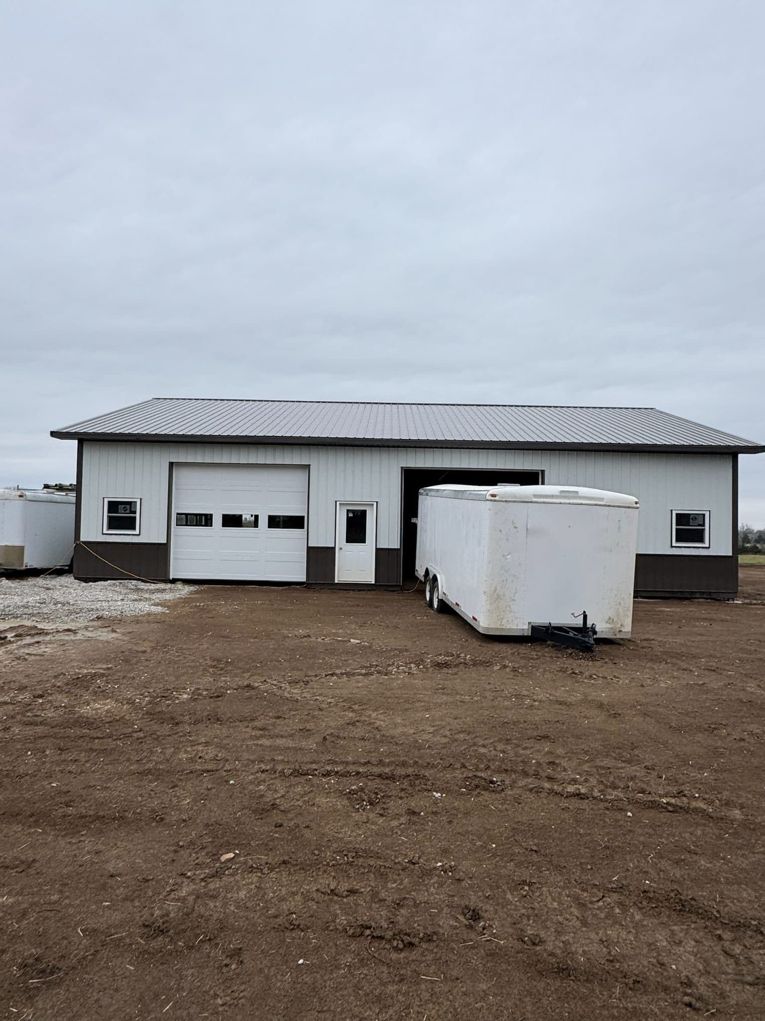 White steel siding with dark trim and wainscot around overhead doors on a post-frame building